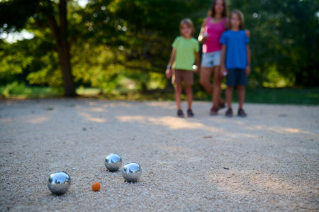 A family plays petanque in a sunny park. The mother watches as her two sons throw metal balls towards the target, enjoying a casual outdoor activity togetherの写真素材