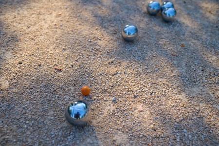 Close-up of petanque balls scattered on gravel with the target ball in focus. The shiny metal balls reflect sunlight, capturing a playful outdoor moment in a park settingの写真素材