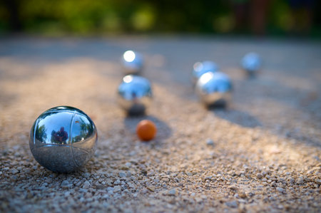 Close-up of petanque balls scattered on gravel with the target ball in focus. The shiny metal balls reflect sunlight, capturing a playful outdoor moment in a park settingの写真素材