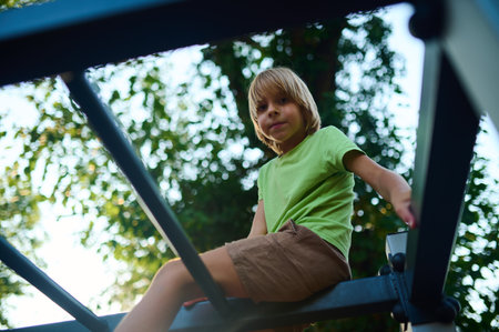 A child plays on a climbing frame in a sunny park surrounded by lush trees during a warm afternoonの写真素材