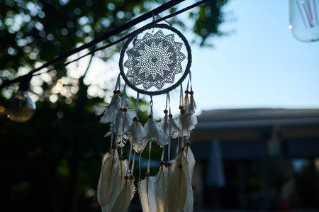 A decorative dreamcatcher hanging in a serene outdoor setting under soft sunlight