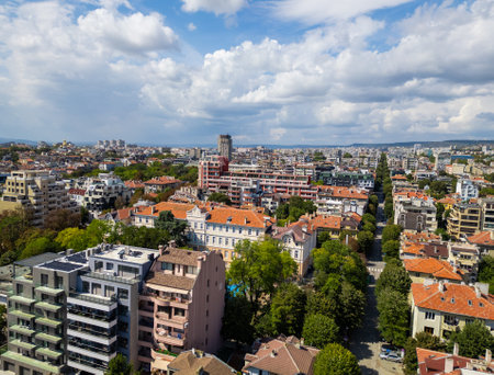 Aerial view of a vibrant cityscape with residential buildings and green trees under a blue sky filled with clouds. Varna Bulgariaの写真素材
