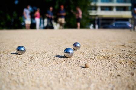 Close-up of petanque balls scattered on gravel with the target ball in focus. The shiny metal balls reflect sunlight, capturing a playful outdoor moment in a park settingの写真素材