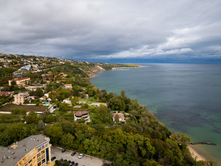 An aerial view of a coastal landscape with a sandy beach, lush green cliffs, and calm waters stretching into the horizon under a cloudy sky. Perfect for travel, nature, or coastal themes.の写真素材