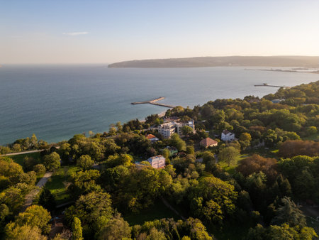 Aerial view of a seaside area with modern buildings, lush greenery, and the calm blue sea in the background. The golden hour light enhances the peaceful urban and coastal landscapeの写真素材