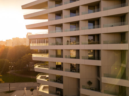 Modern high-rise building at sunset, featuring glass balconies and a tranquil urban setting. The golden hour lighting adds warmth to the minimalistic architecture. Shot with a droneの写真素材