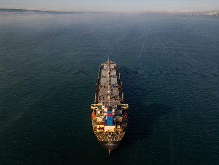 Aerial drone footage of a cargo ship sailing on misty waters with sunlight reflections, creating a calm and mysterious maritime scene, perfect for industrial and nautical themesの写真素材