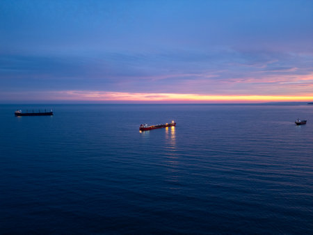 Serene sunset over calm sea with cargo ships illuminated by golden light, creating a tranquil maritime atmosphereの写真素材