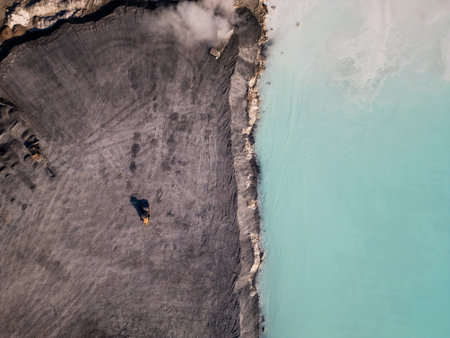 A cement factory tailings site with heavy machinery operating near a turquoise lake. Trucks and bulldozers move materials across the barren, gray terrain, highlighting industrial processes and environmental impactの写真素材