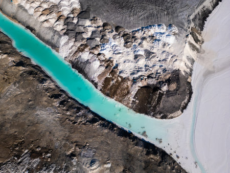 A striking contrast between turquoise water and dark, rugged terrain at a tailings lake. The industrial site reveals layers of environmental impact, blending sharp textures with vivid colorsの写真素材