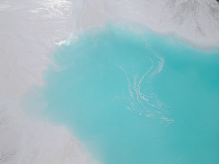 A turquoise tailings pond near a cement factory, surrounded by rugged hills. The vivid water contrasts with the barren land, creating a striking yet industrial scene of environmental impactの写真素材