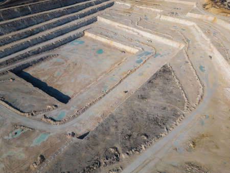 An open-pit quarry with terraced layers and heavy machinery operating on the dusty terrain. The industrial site highlights large-scale excavation processes and environmental transformationの写真素材