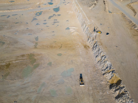 An open-pit quarry with terraced layers and heavy machinery operating on the dusty terrain. The industrial site highlights large-scale excavation processes and environmental transformationの写真素材