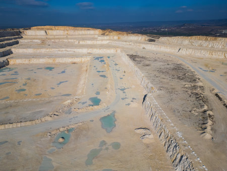 An open-pit quarry with terraced layers and heavy machinery operating on the dusty terrain. The industrial site highlights large-scale excavation processes and environmental transformationの写真素材