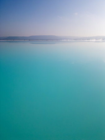 A turquoise pond surrounded by rugged hills. The vivid water contrasts with the barren land, creating a striking yet industrial scene.の写真素材