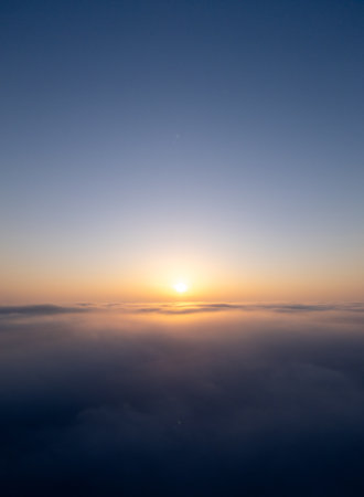 Sunrise above a vast sea of clouds. The golden light gently illuminates the misty sky, creating a dreamlike, tranquil atmosphere with soft colors and smooth motion. Aerial drone viewの写真素材