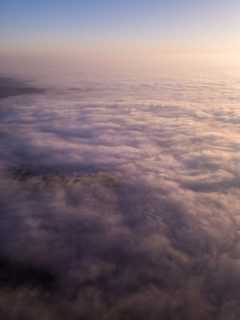 A breathtaking aerial view of sunrise above a vast sea of clouds. The golden light casts a soft glow over rolling mist, creating a dreamy, tranquil atmosphere with smooth motion and a high-altitude perspectiveの写真素材