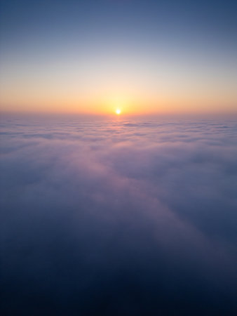 Sunrise above a vast sea of clouds. The golden light gently illuminates the misty sky, creating a dreamlike, tranquil atmosphere with soft colors and smooth motion. Aerial drone viewの写真素材