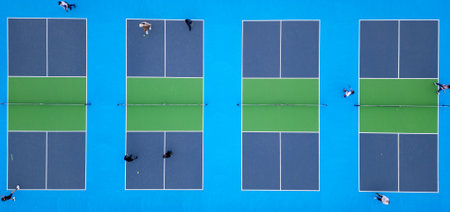 Aerial top-down view of multiple pickleball courts with players engaged in a match. The vibrant blue and green surfaces create a striking geometric pattern, capturing the dynamic movement and energy of the gameの写真素材