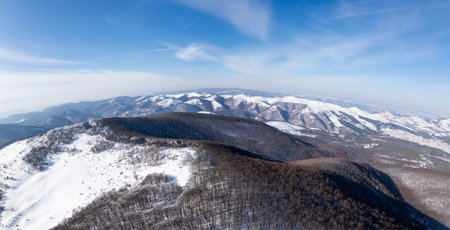 Aerial view of the snow-covered Balkan Mountains in Bulgaria. The winter landscape features rolling hills, frost-covered trees, and a clear blue sky. Hikers walk through the serene wildernessの写真素材
