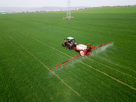 Tractor spraying fertilizer or pesticide on a large green field during spring, demonstrating modern agricultural technology and crop careの写真素材