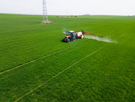 Tractor spraying fertilizer or pesticide on a large green field during spring, demonstrating modern agricultural technology and crop careの写真素材