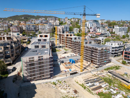 Modern residential buildings under construction with scaffolding and cranes, captured on a clear sunny dayの写真素材