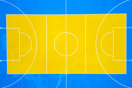 Aerial view of a colorful outdoor basketball court with vibrant blue and yellow markings, two hoops, and symmetrical layout. Shot from directly above.の写真素材