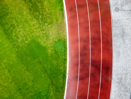 Aerial view of a red running track with marked lanes and curved lines. Athletic stadium section with part of a green football field.の写真素材