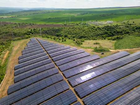 Aerial view of a large solar power farm with rows of photovoltaic panels set in a rural landscape,...