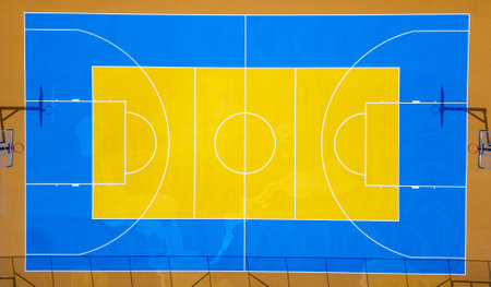Aerial view of a colorful outdoor basketball court with vibrant blue and yellow markings, two hoops,...