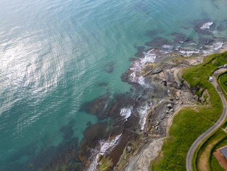 Aerial top-down view of turquoise sea waves crashing over rocky coastline with moss and clear water. Wild nature texture along the Bulgarian coast, dramatic and scenicの写真素材