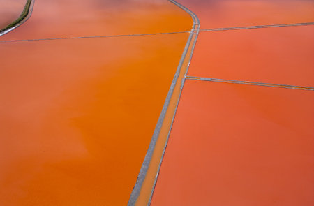 Aerial view of colorful salt pans near Burgas, Bulgaria. Vibrant red and orange evaporation ponds contrast with white salt piles and turquoise sea. Industrial and natural beauty combinedの写真素材