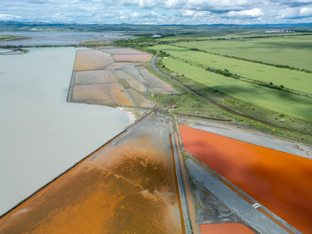 Aerial view of colorful salt pans near Burgas, Bulgaria. Vibrant red and orange evaporation ponds contrast with white salt piles and turquoise sea. Industrial and natural beauty combinedの写真素材