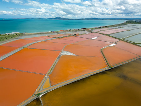 Aerial view of colorful salt pans near Burgas, Bulgaria. Vibrant red and orange evaporation ponds contrast with white salt piles and turquoise sea. Industrial and natural beauty combinedの写真素材