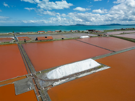 Aerial view of colorful salt pans near Burgas, Bulgaria. Vibrant red and orange evaporation ponds contrast with white salt piles and turquoise sea. Industrial and natural beauty combinedの写真素材