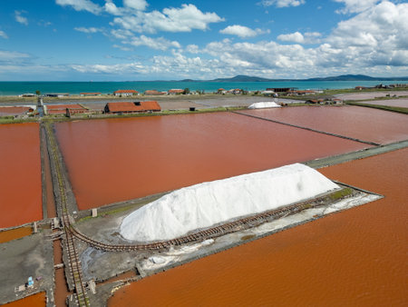 Aerial view of colorful salt pans near Burgas, Bulgaria. Vibrant red and orange evaporation ponds contrast with white salt piles and turquoise sea. Industrial and natural beauty combinedの写真素材
