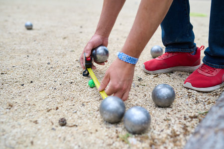 A player measures the distance between boules and the jack on a petanque court using a measuring tape during a competitive matchの写真素材