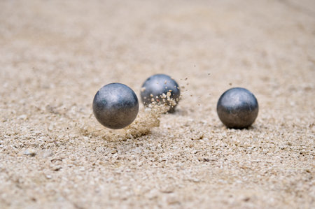 Flying petanque ball hits the ground, sending gravel into the air during a dynamic throw in a...