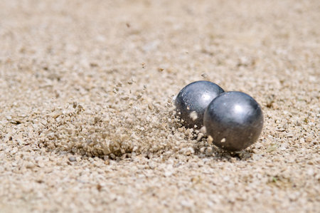 Flying petanque ball hits the ground, sending gravel into the air during a dynamic throw in a competitive match on a sandy terrainの写真素材