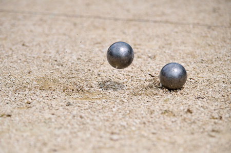Flying petanque ball hits the ground, sending gravel into the air during a dynamic throw in a...