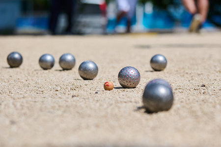 Close-up of petanque balls and jack on a sandy court during a game, with a player standing in the background. Competitive outdoor sport with focus on precisionの写真素材