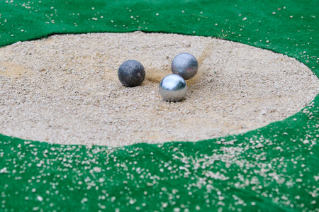Petanque precision shooting competition moment with metal balls hitting target in sand, dust flying on impact. Focus on accuracy and dynamic playの写真素材