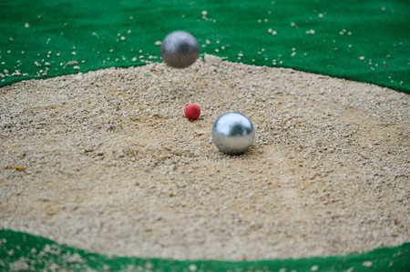 Petanque precision shooting competition moment with metal balls hitting target in sand, dust flying on impact. Focus on accuracy and dynamic playの写真素材