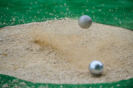 Petanque precision shooting competition moment with metal balls hitting target in sand, dust flying on impact. Focus on accuracy and dynamic playの写真素材