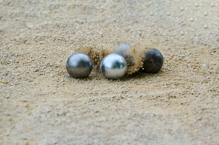 Close-up of petanque precision shooting moment with metal ball hitting target boule, sand and dust...