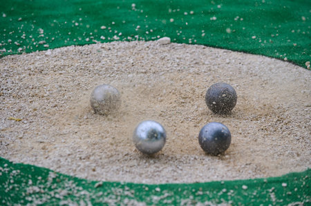 Petanque precision shooting competition moment with metal balls hitting target in sand, dust flying on impact. Focus on accuracy and dynamic playの写真素材