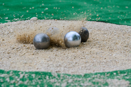 Petanque precision shooting competition moment with metal balls hitting target in sand, dust flying on impact. Focus on accuracy and dynamic playの写真素材