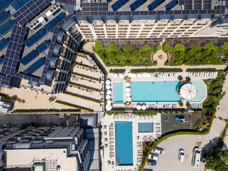 Aerial top-down view of a luxury hotel complex with solar panels, swimming pools, sunbeds, gardens, and a playground. Modern sustainable resort with elegant landscaping and amenitiesの写真素材