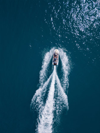 Aerial view of a jet ski speeding across dark blue water, leaving a dynamic white trail. Captured by drone from above, showcasing motion, power, and summer fun on the seaの写真素材